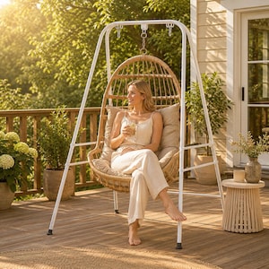 May include: A white metal A-frame stand supporting a hanging egg-shaped chair made of woven light brown wicker. The chair features a plush beige cushion and is suspended by a metal chain. The structure is designed for outdoor seating.