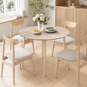 May include: A round dining table with a light wood grain finish and four matching chairs featuring light wood frames and upholstered light gray seats. A glass vase with white roses and a bowl of oranges sit on the table surface.