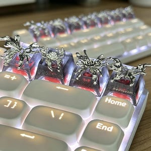 May include: A mechanical keyboard featuring custom artisan keycaps with translucent dark purple resin bases containing glitter and red accents, topped with intricate silver-toned metal butterfly and floral embellishments.