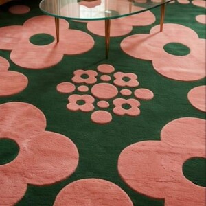 May include: A dark green area rug featuring a repeating pattern of large, soft pink flower shapes with circular centres. A central cluster of smaller pink flowers and circles is positioned between the larger floral motifs on the rug surface.
