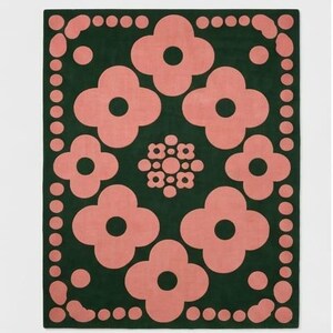 May include: A rectangular area rug featuring a dark forest green background with a repeating pattern of large, light pink four-petaled flower shapes. The border consists of a series of light pink circles and rounded shapes framing the central design.