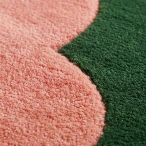 May include: A close-up view of a tufted textile surface featuring a distinct curved boundary between a soft, light pink section and a deep forest green section. The material has a dense, looped pile texture that creates a tactile, fuzzy appearance.