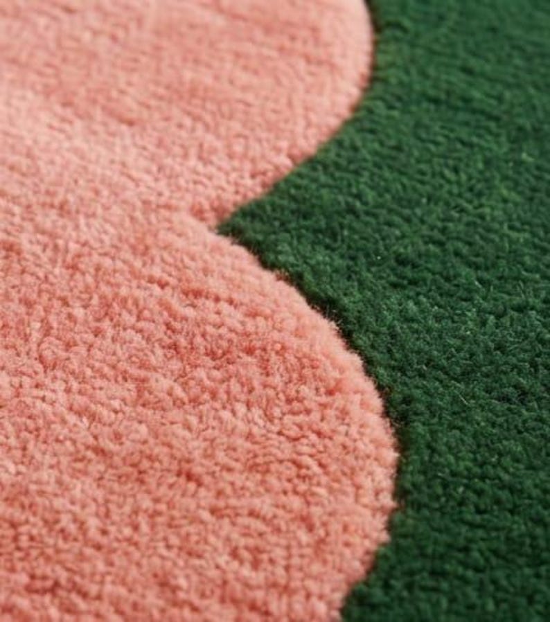 May include: A close-up view of a tufted textile surface featuring a distinct curved boundary between a soft, light pink section and a deep forest green section. The material has a dense, looped pile texture that creates a tactile, fuzzy appearance.