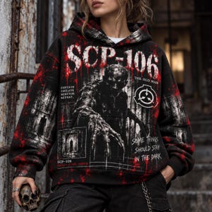 Op de afbeelding: Een zwarte hoodie met een grafische print van SCP-106, The Old Man. Het ontwerp bevat rode spetterpatronen, de tekst SCP-106, The Old Man, Contain, Isolate, Monitor, Repeat en Some Things Should Stay In The Dark.