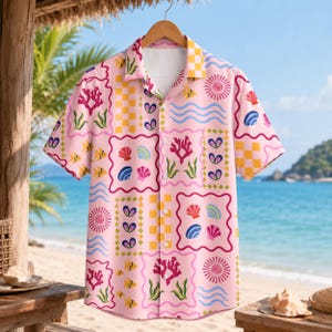 Puede incluir: Una camisa de manga corta con botones en color rosa claro que presenta un patrón de mosaico repetitivo de cuadrados a cuadros amarillos, coral rosa, conchas azules y rosas, peces amarillos y líneas onduladas azules, con cuello clásico.