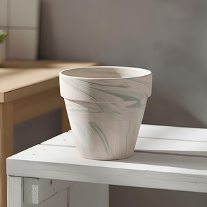 Pode incluir: Um vaso de plantas cônico com um padrão marmorizado com redemoinhos de branco suave e verde sálvia suave. O recipiente tem um acabamento fosco liso e uma borda distinta no topo, exibindo uma forma cilíndrica limpa e funcional.