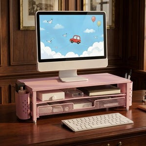 May include: A light pink metal monitor stand with a mesh shelf and a pull-out drawer. The stand features side compartments for stationery storage and supports a computer monitor displaying a blue sky with a red car and balloons.