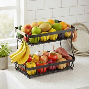 May include: A two-tier black metal wire storage basket filled with assorted fresh produce. The top tier holds apples, pears, lemons, and limes. The bottom tier contains a bunch of yellow bananas, red tomatoes, yellow and red bell peppers, onions, garlic, and potatoes.