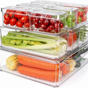 May include: A set of clear plastic rectangular food storage containers stacked in multiple tiers. The containers hold various fresh produce including red cherry tomatoes, red grapes, green grapes, strawberries, celery stalks, corn, and carrots.