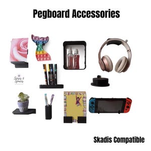 May include: A collection of black pegboard accessories including shelves, pen holders, and hooks. Items displayed include a rose print, a rainbow whale fidget toy, spray bottles, headphones, a small potted plant, pens, a notepad, and a game console.