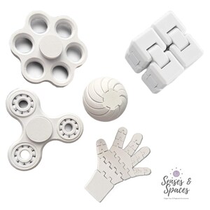 May include: A collection of five white sensory fidget toys including a flower-shaped spinner, a rectangular infinity cube, a three-pronged spinner with visible ball bearings, a textured sphere, and a hand-shaped articulated toy. Text reads Senses & Spaces.