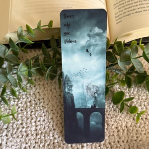 May include: A rectangular bookmark featuring a dark, atmospheric landscape with a stone bridge, silhouetted figures, and birds in a cloudy sky. The text "There's only you, Violence." is printed in a dark script font at the top of the bookmark.