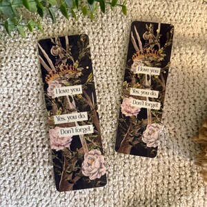 May include: Two rectangular bookmarks featuring a dark floral design with white peonies, branches, and a gold crown. Each bookmark displays the text: I love you, Yes, you do, Don't forget, printed on white rectangular labels against the dark background.