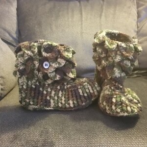 Puede incluir: Un par de zapatillas de crochet con estampado de camuflaje y botones marrones. Las zapatillas tienen un dise&ntilde;o texturizado y escamoso.