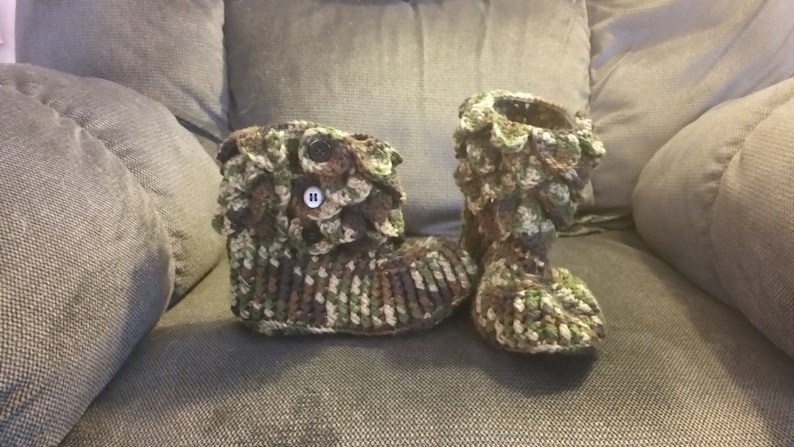 Puede incluir: Un par de zapatillas de crochet con estampado de camuflaje y botones marrones. Las zapatillas tienen un dise&ntilde;o texturizado y escamoso.