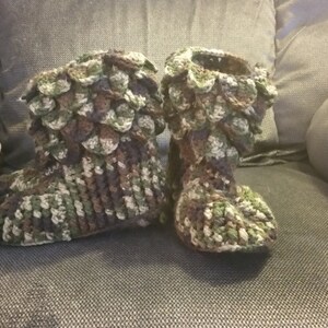 Puede incluir: Un par de zapatillas de crochet en un patr&oacute;n de camuflaje. Las zapatillas est&aacute;n hechas con un dise&ntilde;o texturizado, similar a escamas.