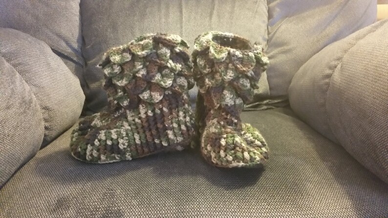 Puede incluir: Un par de zapatillas de crochet en un patr&oacute;n de camuflaje. Las zapatillas est&aacute;n hechas con un dise&ntilde;o texturizado, similar a escamas.