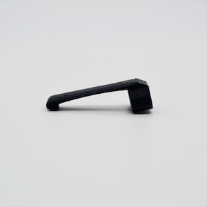 Peut inclure: Un clip noir en forme de L avec une surface texturée. L'objet présente un long bras légèrement incliné s'étendant à partir d'une base rectangulaire plus épaisse. Le design est simple et fonctionnel, avec une finition mate et une couleur noire.