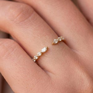 Peut inclure: Une bague ouverte en or ornée d'une série de petites pierres transparentes taille marquise disposées le long de l'anneau. La bague présente une ouverture sur le dessus, avec les pierres agencées en un motif linéaire délicat suivant la courbe.