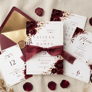 Puede incluir: Un conjunto de papelería de boda con tarjetas blancas decoradas con rosas color burdeos y bordes dorados. El set incluye una invitación atada con una cinta de gasa burdeos, un menú y tarjetas de mesa, presentados con un sobre a juego.