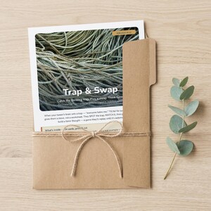May include: A white card game instruction sheet titled Trap & Swap featuring a photo of tangled rope, tucked into a brown kraft paper folder tied with twine. The text includes For Ages 9-12, Catch the thinking trap, Play a swap, and What's inside.
