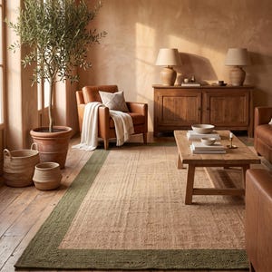 May include: A rectangular area rug featuring a natural tan woven center and a wide, textured olive green border. The rug is laid flat on a wooden floor, showcasing a distinct contrast between the neutral interior and the dark green edge.