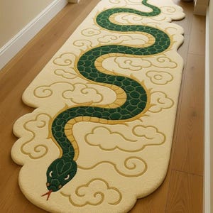 Puede incluir: Una alfombra alargada de color crema con un gran motivo de serpiente sinuosa en verde y amarillo. La serpiente presenta un patrón texturizado de escamas en el lomo y una lengua roja bífida. El diseño está rodeado por contornos de nubes amarillas.
