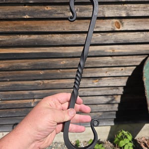 May include: A black metal S-hook featuring a central twisted bar design with curled ends. The hook is constructed from a single piece of dark, forged metal, showcasing a symmetrical shape with a spiral twist in the middle and curved hooks at both ends.