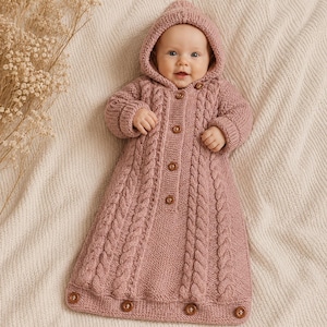 May include: A dusty rose knitted baby bunting bag featuring a hood, long sleeves, and a front button closure. The garment is crafted with a vertical cable knit pattern running down the center and sides, finished with four buttons along the bottom hem.