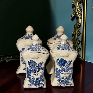 Può includere: Un set di quattro barattoli per spezie in ceramica color crema con motivi floreali blu e coperchi abbinati. Due barattoli presentano etichette con il testo Sel e Poivre in caratteri neri. Ogni barattolo ha una sezione superiore testurizzata.