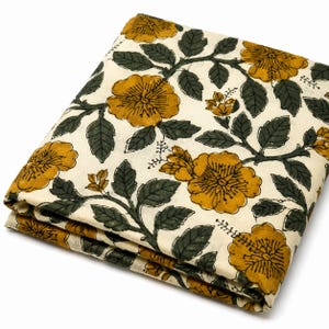 Puede incluir: Una pieza de tela plegada de color blanco roto con un patrón floral repetitivo. El diseño consiste en flores de color amarillo mostaza con hojas y tallos de color verde oscuro, dispuestos en un estampado botánico continuo sobre la superficie.