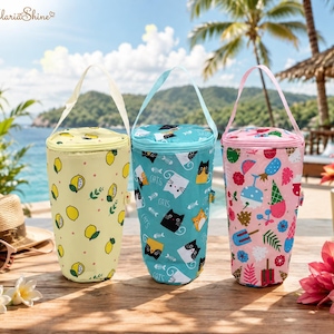 May include: Three cylindrical insulated bags with carrying straps. The left bag is yellow with a lemon pattern, the centre bag is teal with a cat and fish bone print, and the right bag is pink with a colourful ice cream and fruit pattern.