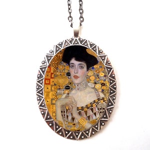 May include: A silver oval pendant necklace with a portrait of a woman in a gold and white dress. The portrait is surrounded by a silver frame with a geometric pattern.