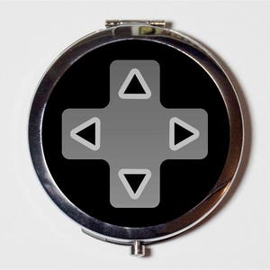 May include: A silver compact mirror with a black background and a gray directional pad, similar to a video game controller.