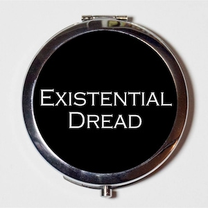 May include: A silver compact mirror with a black background and the text "EXISTENTIAL DREAD" in white.