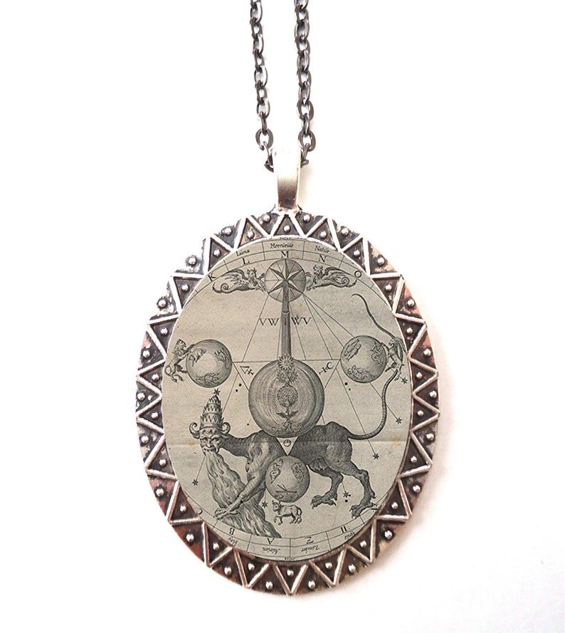 May include: A silver pendant necklace with a round, antique-style design. The pendant features a black and white illustration of a mythical creature with a human head and a lion's body, surrounded by a circle of stars and planets. The pendant is framed by a silver border with a repeating pattern of triangles.