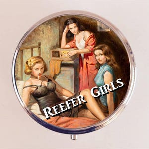 May include: A vintage style compact mirror with a colorful illustration of three women in a bedroom setting. The text "REEFER GIRLS" is printed on the mirror.
