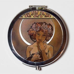 Peut inclure: Un miroir compact argenté avec un motif Art nouveau coloré représentant une femme avec une couronne de fleurs et un croissant de lune en arrière-plan.