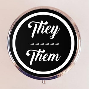 May include: A round, silver compact mirror with a black and white design. The design features the words "They" and "Them" in a white, cursive font on a black background.