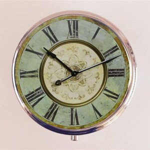 May include: A silver-toned round clock with Roman numeral markings and a distressed green face. The clock has a decorative floral design in the center.