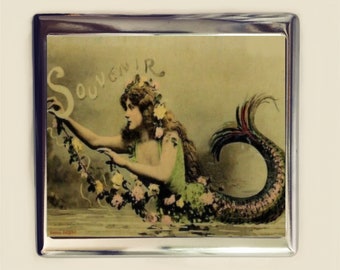 May include: A vintage silver cigarette case with a colorful image of a mermaid with a green tail and a floral crown. The image has the word "Souvenir" written in cursive.