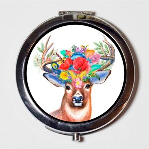 May include: A silver compact mirror with a colorful floral design on the lid. The design features a deer with antlers and a crown of flowers in shades of pink, red, blue, yellow, and green.