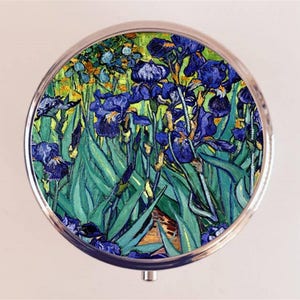 May include: A round, silver compact mirror with a colorful image of a painting of blue irises with green leaves. The painting is by Vincent van Gogh.