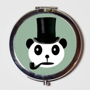 May include: A silver compact mirror with a green background and a black and white panda wearing a black top hat and smoking a pipe.