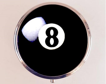May include: A black and white 8 ball design on a round, silver-colored pill box.
