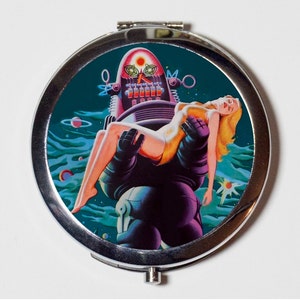 May include: A silver compact mirror with a colorful image of a robot holding a woman in a yellow dress. The background is a teal blue with stars and planets.