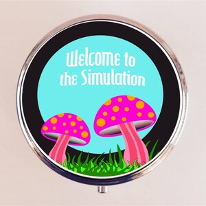 May include: A round, silver-colored pill box with a black background and a blue circle in the center. The blue circle has the text "Welcome to the Simulation" and two pink and yellow mushrooms with white dots.