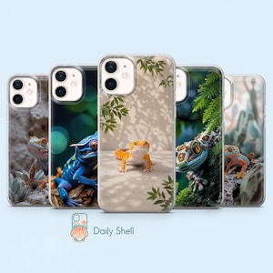 Puede incluir: Cinco fundas transparentes para smartphone con varios diseños de geckos. Los diseños incluyen un gecko sobre una roca, un gecko azul, un gecko naranja bajo luz moteada, un gecko sobre una rama con musgo y un gecko sobre una superficie texturizada.