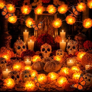 May include: A Day of the Dead altar featuring multiple decorated sugar skulls, round sweet breads, and lit candles. A string of glowing orange marigold-shaped lights is draped across the scene, accented by several monarch butterfly ornaments.