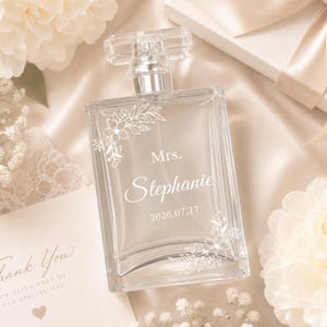 May include: A clear glass perfume bottle with a rectangular shape and a transparent cap. The front features white etched floral designs in the corners, with the text Mrs. Stephanie and the date 2026.07.17 printed in the centre.